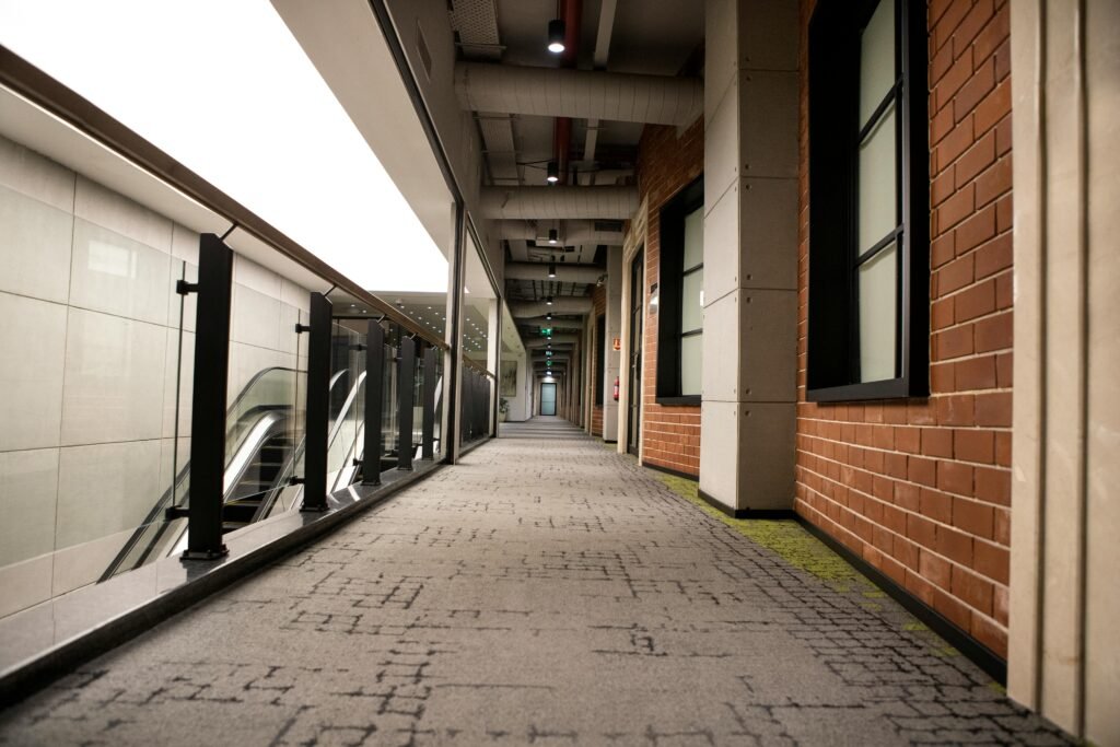 A modern indoor hallway featuring brick walls and carpet flooring, with escalators and handrails.